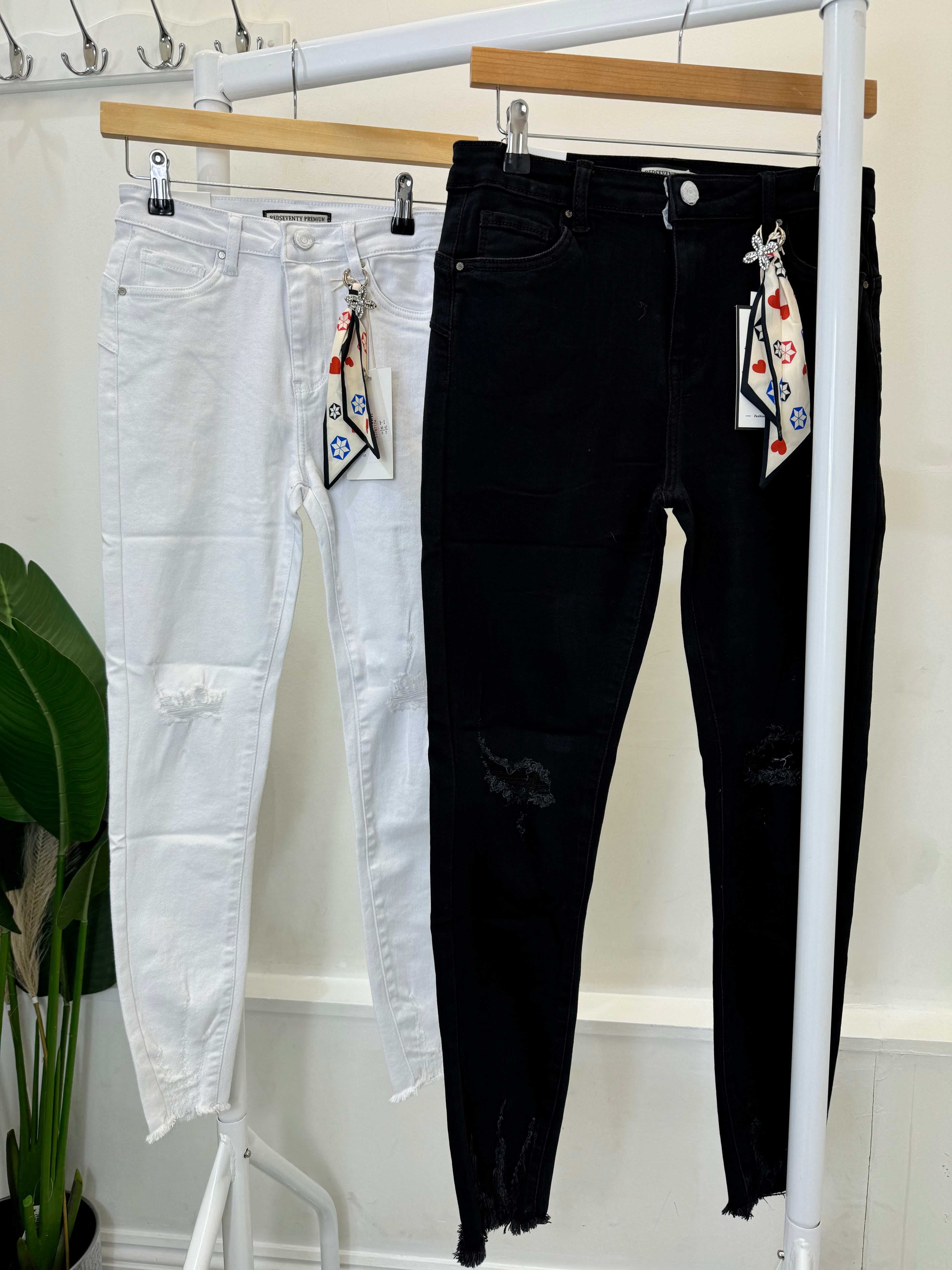 Two pairs of jeans hanging on a rack, one is black and the other is white, both with visible distressed details.